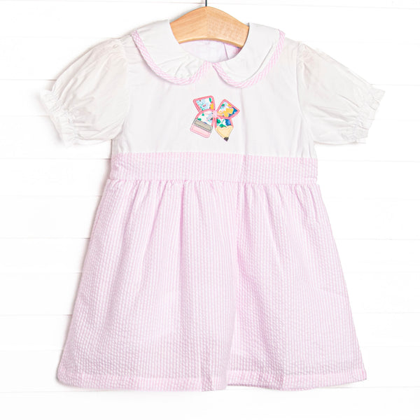  This dress features a pink seersucker material, a Peter Pan collar with pink seersucker trim, and a pencil petal applique. 