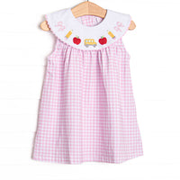  This dress features pink gingham material, embroidered school details, and ric rac trim around the collar. 