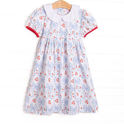 This dress features a white blue bow and apple patterned material, puff sleeves, and red piping trim.