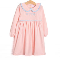 This dress features a pink material, a trio of blue bow embroidery, and a peter pan collar with ruffle trim.