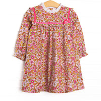 This dress features a fall floral print, ruffle trim, and a pink ribbon.