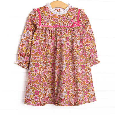 This dress features a fall floral print, ruffle trim, and a pink ribbon.