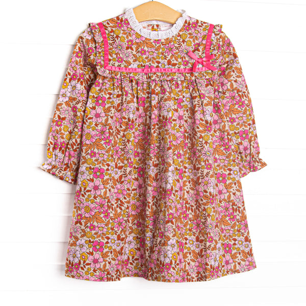 This dress features a fall floral print, ruffle trim, and a pink ribbon.