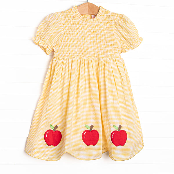This dress features a yellow gingham print, puff sleeves, and apple trio applique.