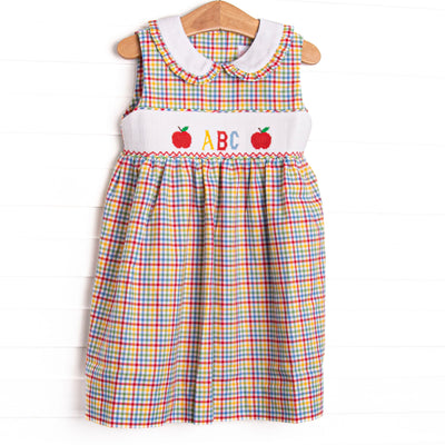 This dress features a multicolored plaid fabric, a Peter Pan plaid ruffle trimmed collar, and ABC and apple smocking.