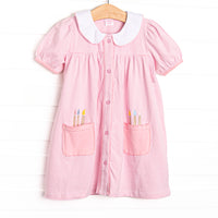 This dress features a pink and white striped fabric, front pickets with paint brush applique, a white collar with pink picot trim, a button down front, and short puff sleeves.