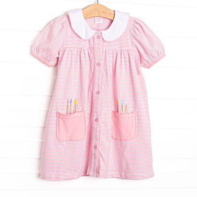 This dress features a pink and white striped fabric, front pickets with paint brush applique, a white collar with pink picot trim, a button down front, and short puff sleeves.