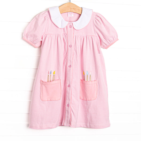 This dress features a pink and white striped fabric, front pickets with paint brush applique, a white collar with pink picot trim, a button down front, and short puff sleeves.