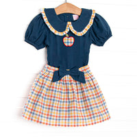 This set features a navy puff sleeve top, a plaid trimmed Peter Pan collar, and a plaid apple applique. Coordinating plaid skirt with a navy bow to match.