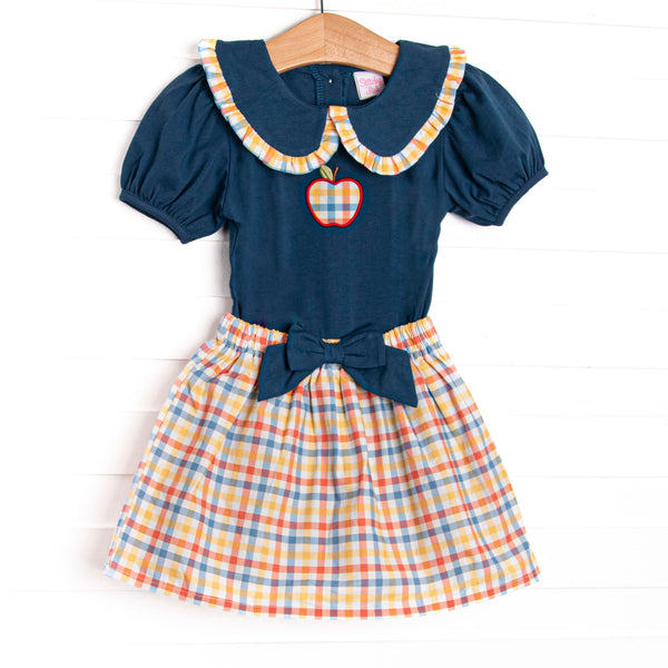 This set features a navy puff sleeve top, a plaid trimmed Peter Pan collar, and a plaid apple applique. Coordinating plaid skirt with a navy bow to match.