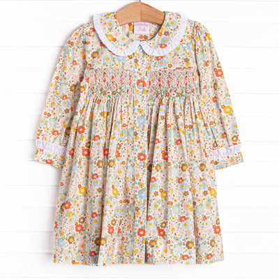 This dress features an orange floral print, a peter pan collar with white ruffle trim, and a dainty smocking.