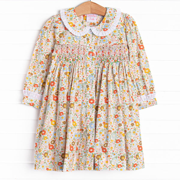 This dress features an orange floral print, a peter pan collar with white ruffle trim, and a dainty smocking.