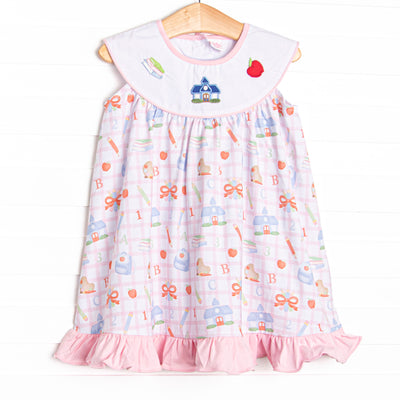 This dress features a pink school inspired print, with a bib collar and&nbsp; school appliques including books, a schoolhouse, and an apple.