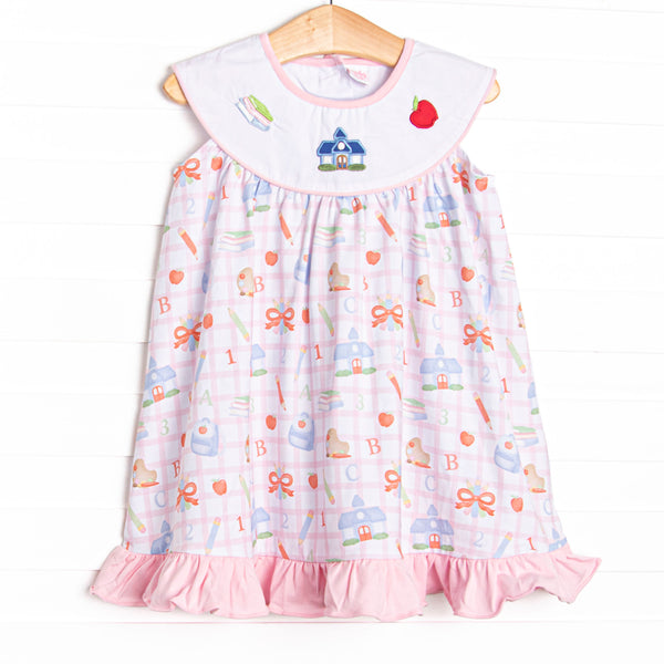 This dress features a pink school inspired print, with a bib collar and&nbsp; school appliques including books, a schoolhouse, and an apple.