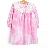  This dress features a pink windowpane print, ruffle collar, and button closure. 