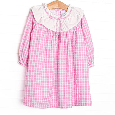  This dress features a pink windowpane print, ruffle collar, and button closure. 