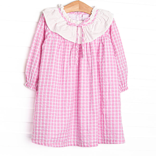  This dress features a pink windowpane print, ruffle collar, and button closure. 