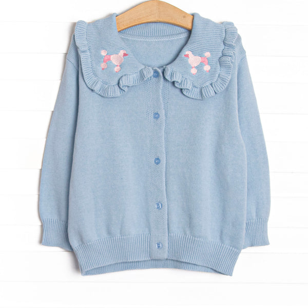  This cardigan features blue knit fabric, pink poodle embroidery, a blue ruffle collar and blue buttons down the front. 