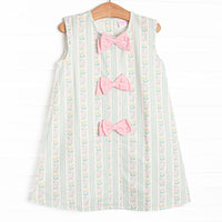 This dress features a green floral print, pink bow details, and button closure on the back.
