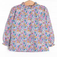  This top features an orange floral print, a hand-tied bow on the neck, and ruffle trim. 