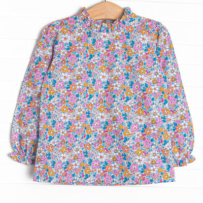  This top features an orange floral print, a hand-tied bow on the neck, and ruffle trim. 