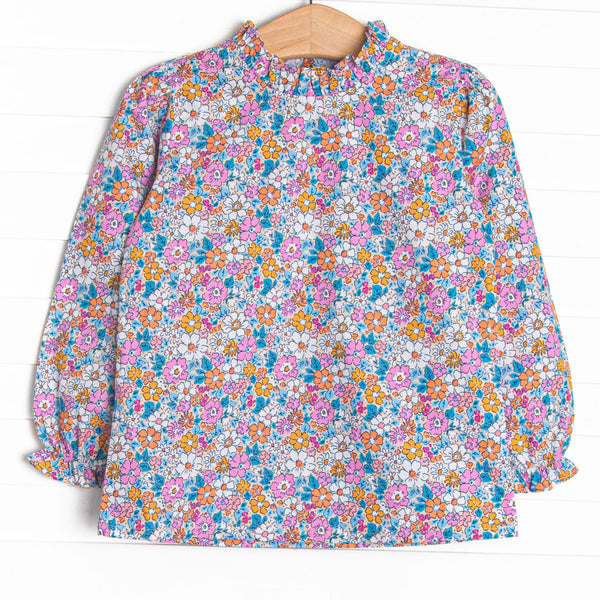  This top features an orange floral print, a hand-tied bow on the neck, and ruffle trim. 