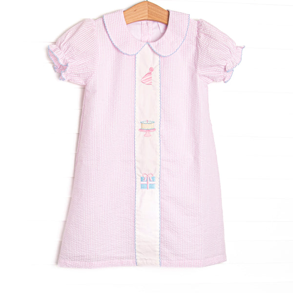 This birthday dress features light pink seersucker fabric, birthday embroidery, a pink Peter Pan collar, and short puff sleeves.