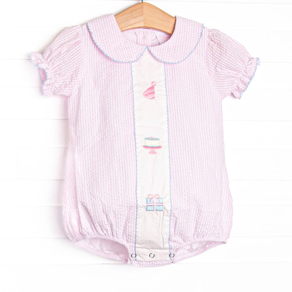 This birthday bubble features light pink seersucker fabric, birthday embroidery, a pink Peter Pan collar, and short puff sleeves.