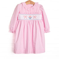 This dress features light pink gingham fabric, bow and cake smocking, ruffle neck trim, and long sleeves.
