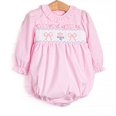 This bubble features light pink gingham fabric, bow and cake smocking, ruffle neck trim, and long sleeves.