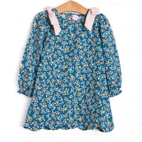  This dress features a blue floral print, long sleeves, a scallop hem, and pink bow shoulders. 