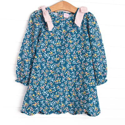  This dress features a blue floral print, long sleeves, a scallop hem, and pink bow shoulders. 