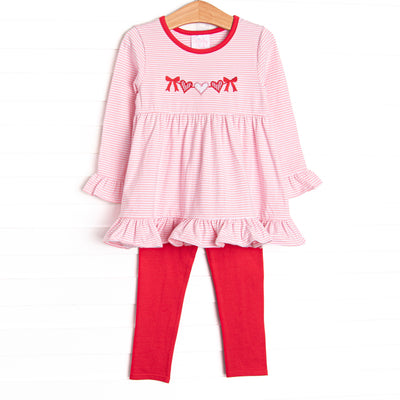 This precious set features a pink striped&nbsp; top with ruffle hem details and a heart string applique. Red leggings to match.