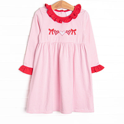 This precious dress features a pink striped print, red ruffle trim details and a heart string applique