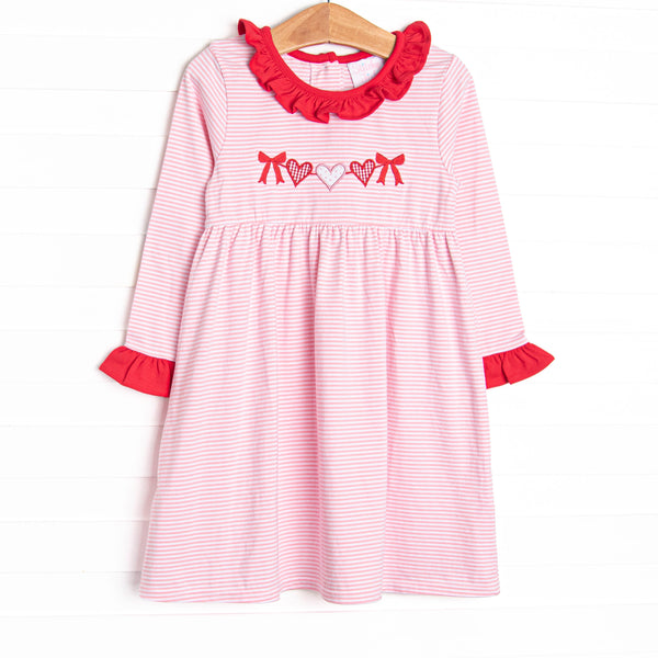 This precious dress features a pink striped print, red ruffle trim details and a heart string applique