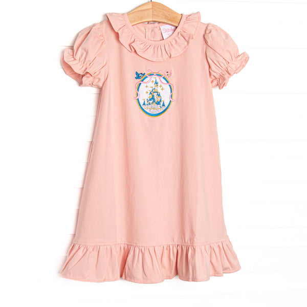 This dress features pink knit material, a framed castle embroidery, and ruffle trim. 