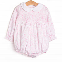 This bubble features a pink toile print, an elastic smocking across the chest, and a peter pan collar.