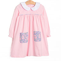 This dress features a pink knit material, purple floral front pockets, and peter pan collar.