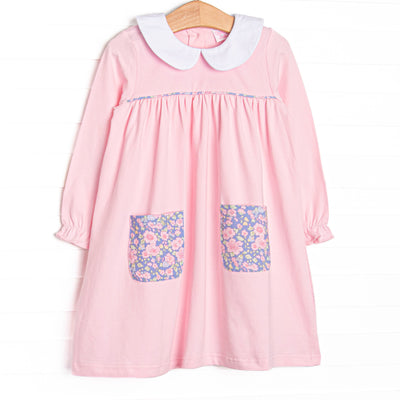 This dress features a pink knit material, purple floral front pockets, and peter pan collar.