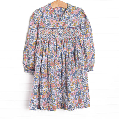  This dress features a navy floral fabric, dainty smocking, and front buttons. 