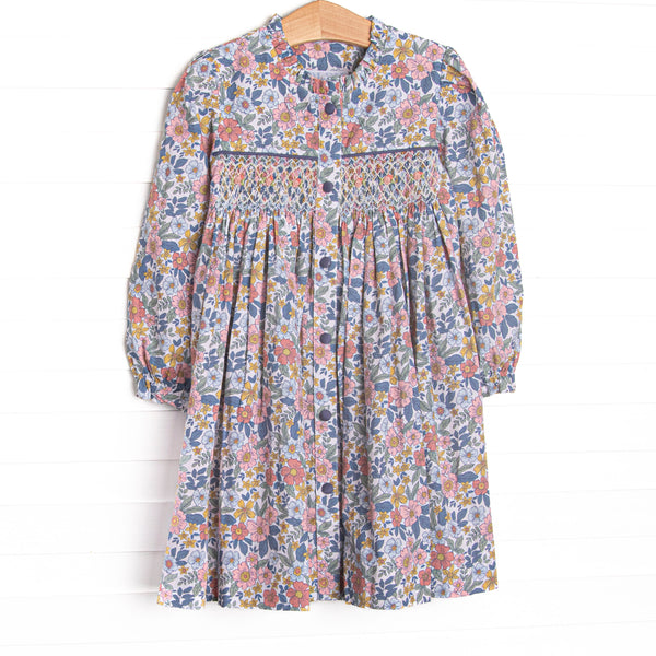  This dress features a navy floral fabric, dainty smocking, and front buttons. 