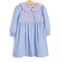 This dress features a blue gingham print, a peter pan collar with pink ruffle trim, and a trio of bow embroideries.