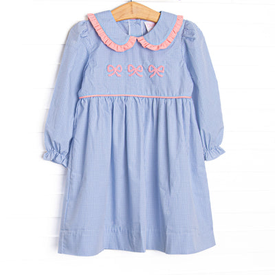 This dress features a blue gingham print, a peter pan collar with pink ruffle trim, and a trio of bow embroideries.
