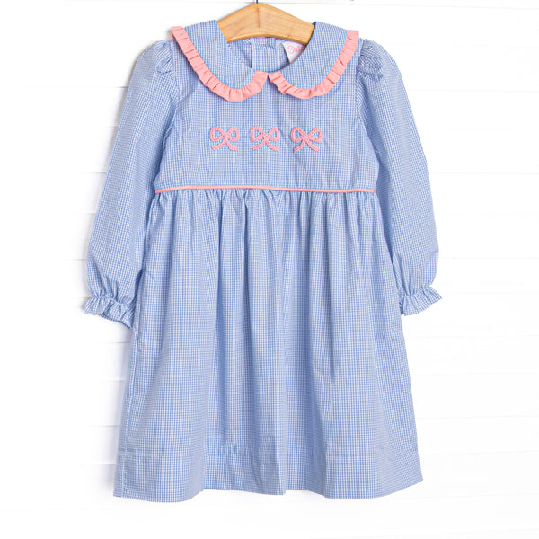 This dress features a blue gingham print, a peter pan collar with pink ruffle trim, and a trio of bow embroideries.