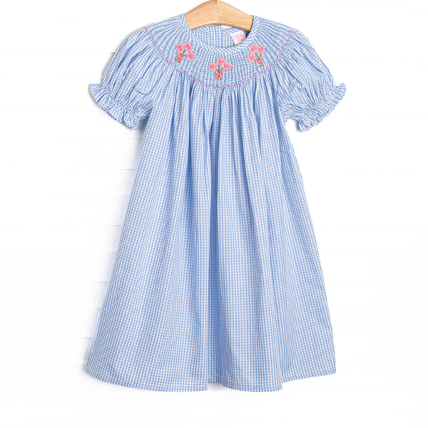 This dress features blue gingham fabric, floral smocking, and short puff sleeves.