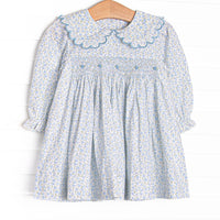 This dress features a blue floral fabric, dainty smocking , and beautiful scalloped trimmed peter pan collar.