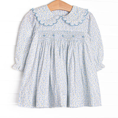 This dress features a blue floral fabric, dainty smocking , and beautiful scalloped trimmed peter pan collar.