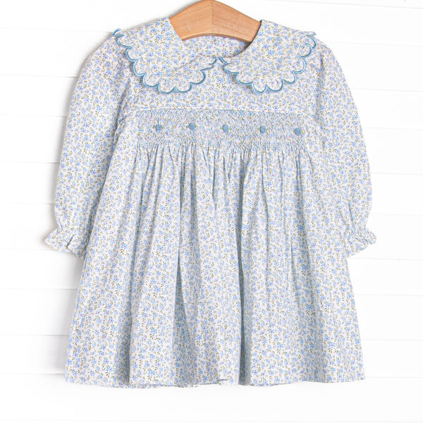 This dress features a blue floral fabric, dainty smocking , and beautiful scalloped trimmed peter pan collar.
