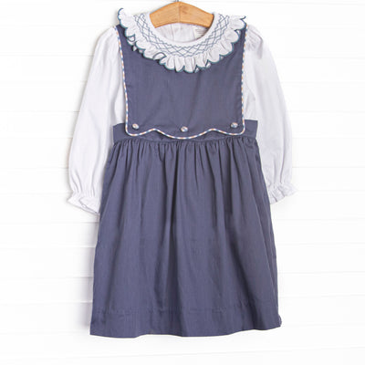  This dress features a navy corduroy fabric, a button on bib, and white long sleeve top with a peter pan collar and ruffle trim. 