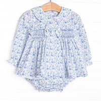 This set features a blue floral fabric, dainty smocking, a floral peter pan collar, and a pre tied bow.